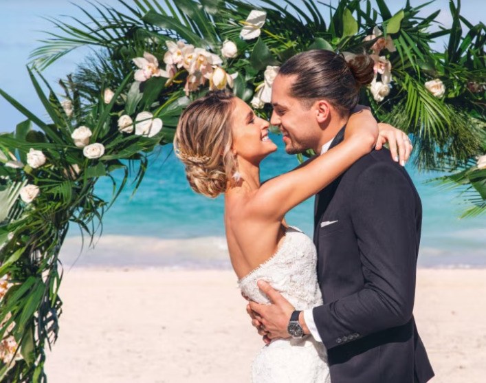 Pareja de recién casados abrazados bajo un arco de flores en la playa